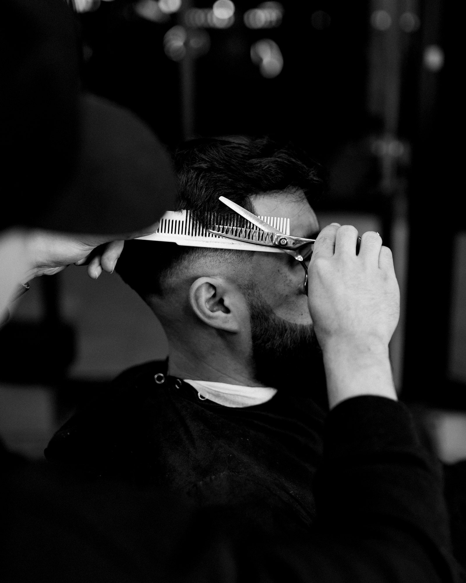 Un homme coupe les cheveux d'un client aux ciseaux, mèche tenue entre les doigts